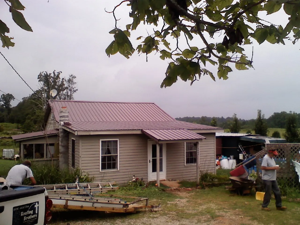 Crew finishing a mauve metal roof on a small farmhouse in Hughesville